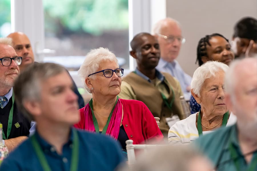 A woman in a red blouse amongst other attendees looking towards the speaker.