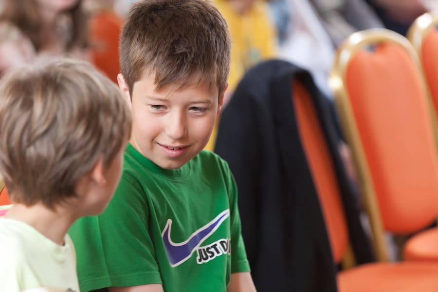 A young boy chatting to another boy in a conference room.