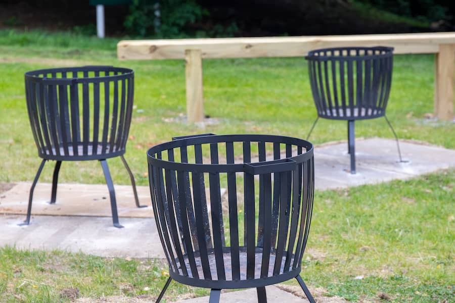 Three black firepits sitting on the grass lawn of high leigh with one of three benches in the background.