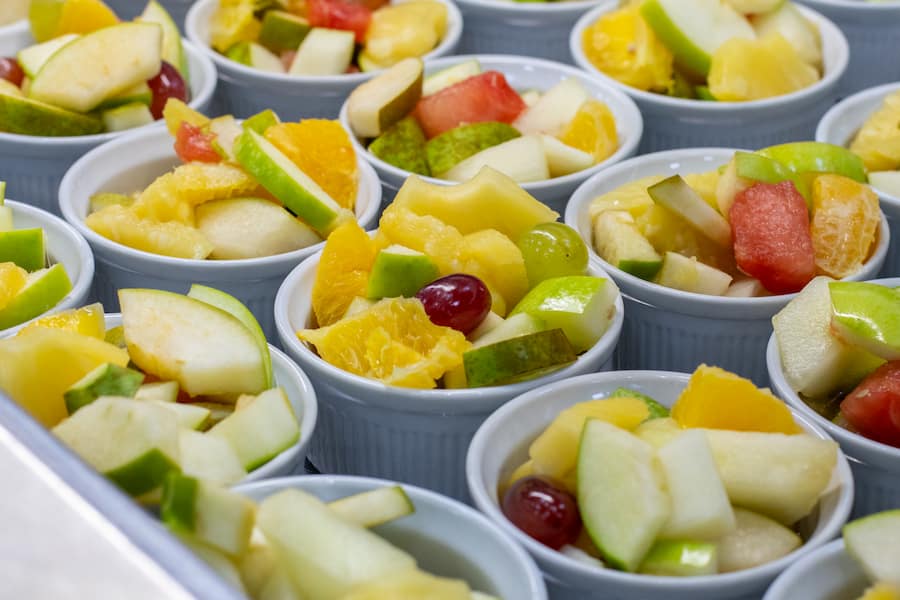 Multiple small bowls of fruit salads including grapes, apples, pineapples and more.