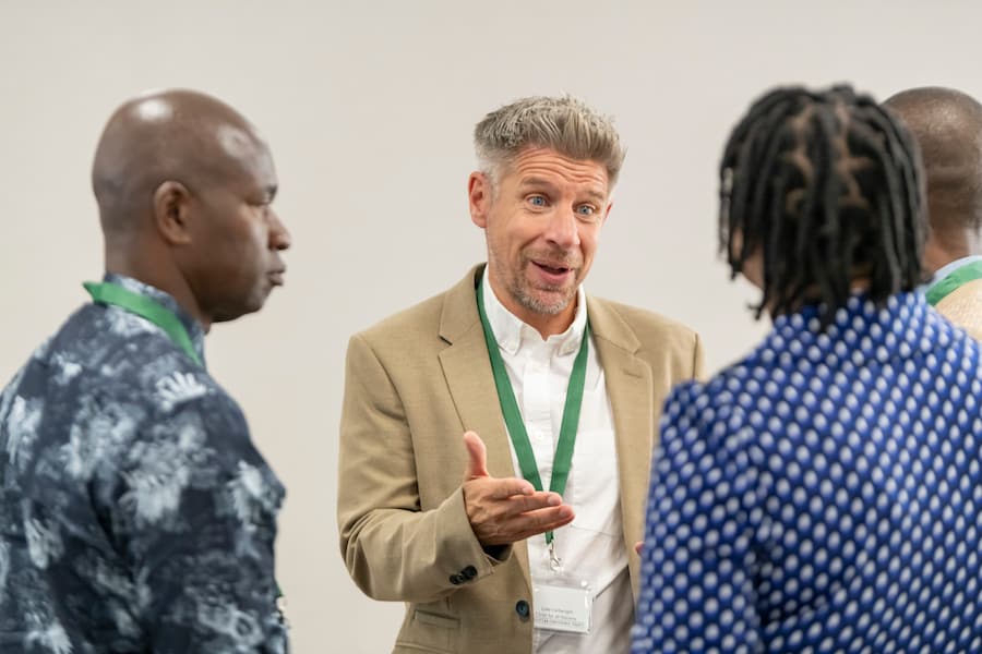 A man in a cream suit talking to three other people at a conference about the theme.
