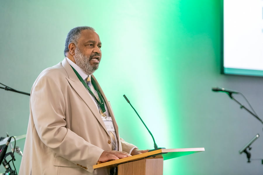 A man in a cream suit speaking at a podium.