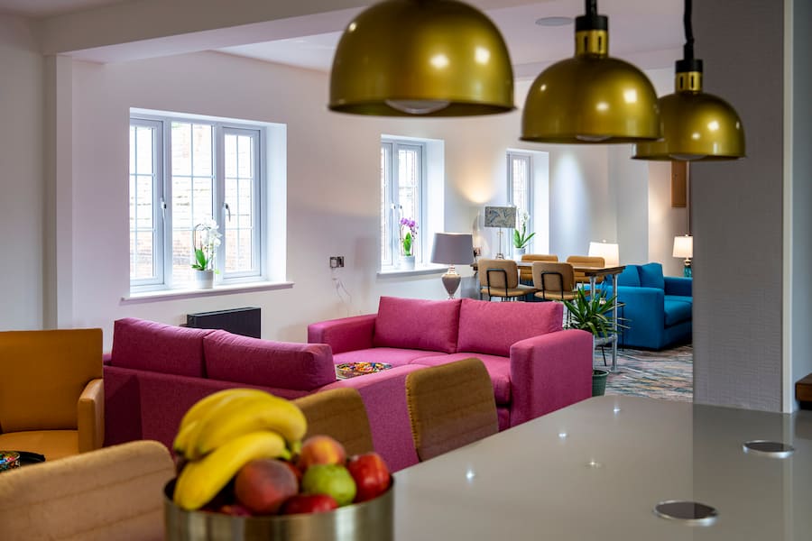 Looking over the counter near the coffee machines in the Ellen Lounge at High Leigh, with pink and blue furniture and a bowl of fruit on the counter.