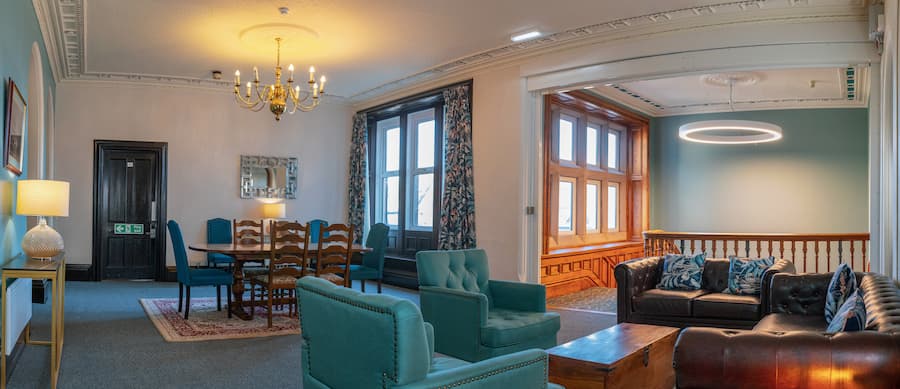 A cosy lounge area with comfy seating, warm lighting with the stairs in the background leading to the Brown Lounge.