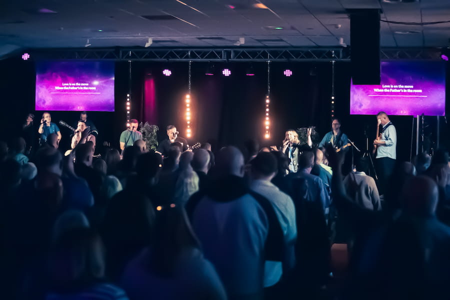 A view of Ground Level Network's worship band on stage in the Derbyshire Hall with a crowd worshipping in dim atmospheric lighting.