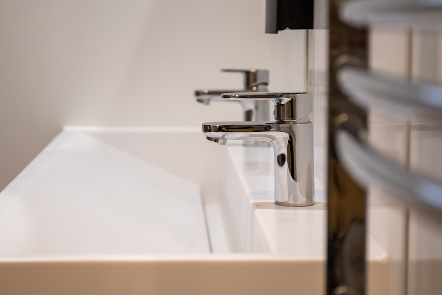 A shiny tap sitting above a brand new sink with a radiator next to it and round mirrors hanging above.