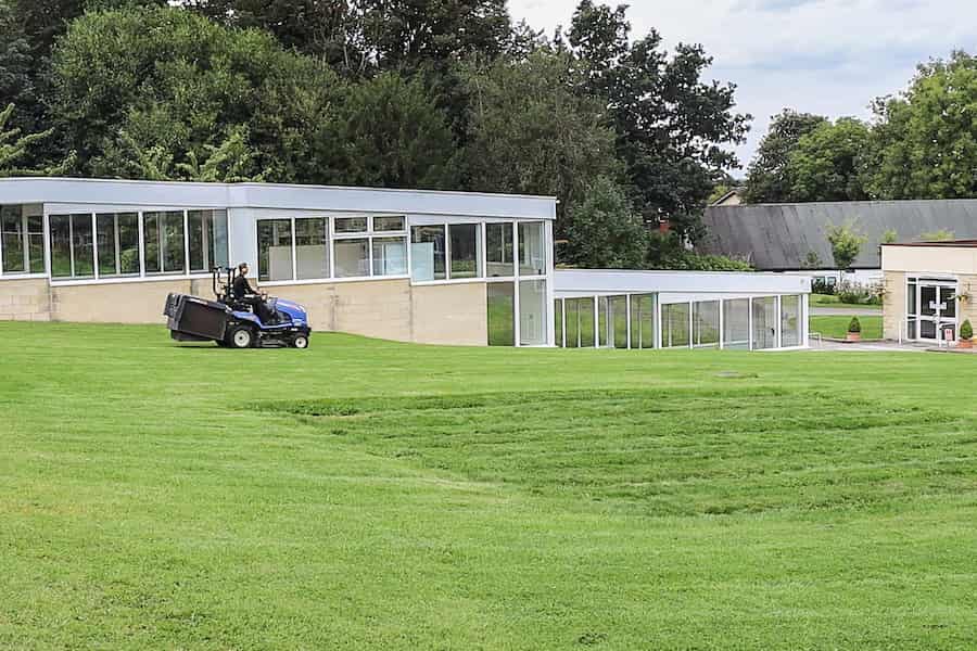 The Hayes' green area next to the Derbyshire Suite with a man on a ride on lawnmower mowing the grass. 