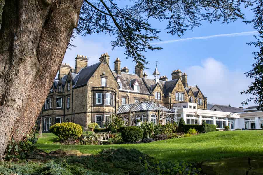 A photograph of The Hayes, showing the beautiful grounds, green grass, and a white bench.