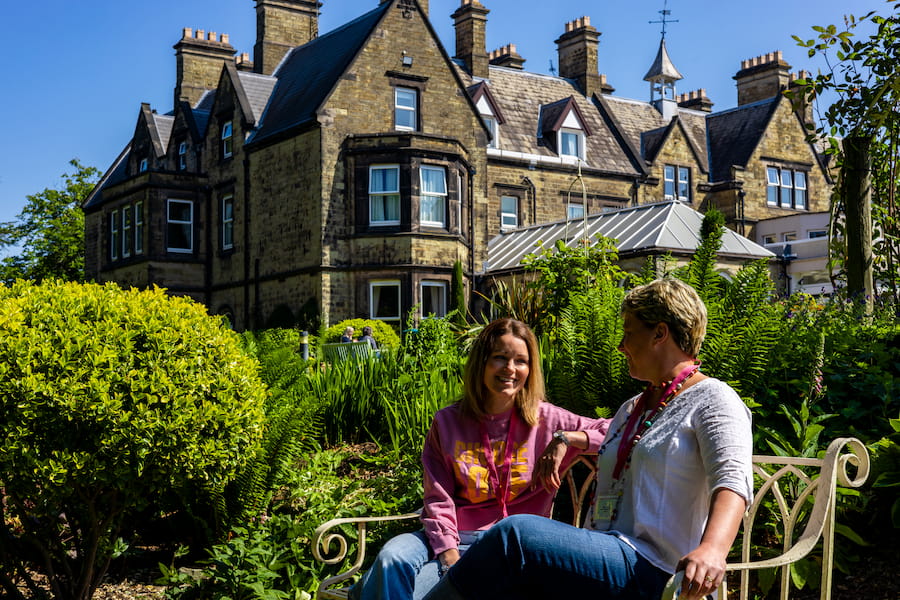 Two leaders sit on a bench outside one of the venues on a sunny day laughing together.