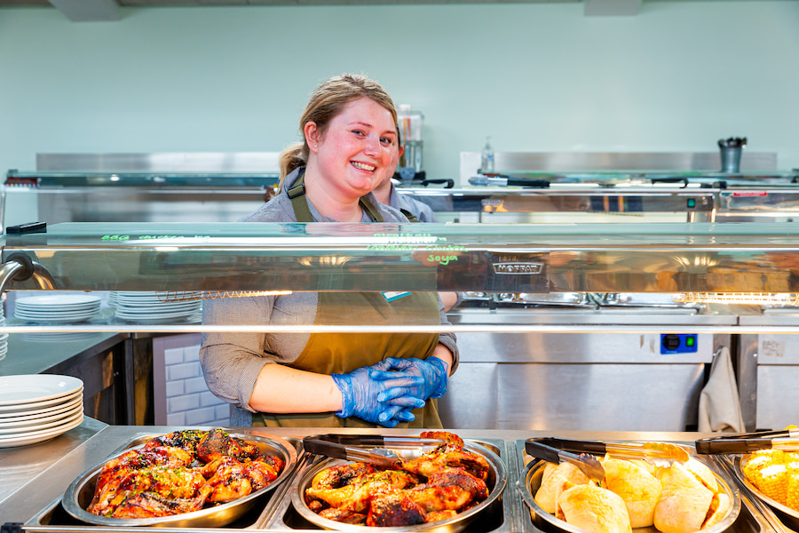 A member of staff at The Hayes smiling at the camera waiting to serve guests in the dining room.
