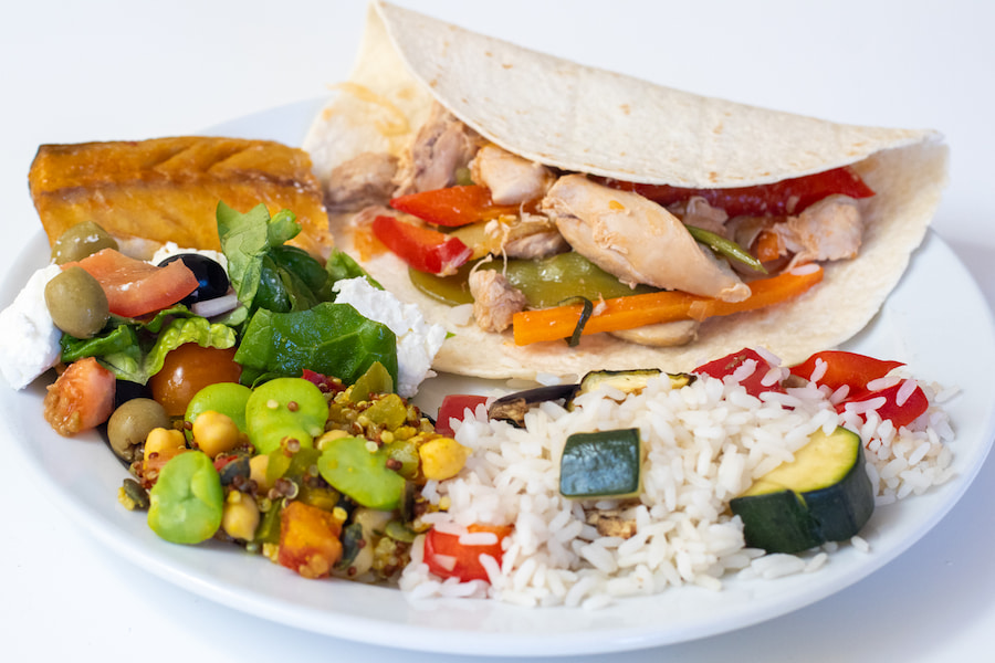 A plate of food at The Hayes showing fajita wraps, a colourful salad, a mackerel fillet, and a side of rice.